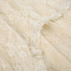 Close-up of delicate off-white silky lace fabric with a floral pattern and a ruffled seam running diagonally across the image. The lace is sheer and has a soft, intricate texture.