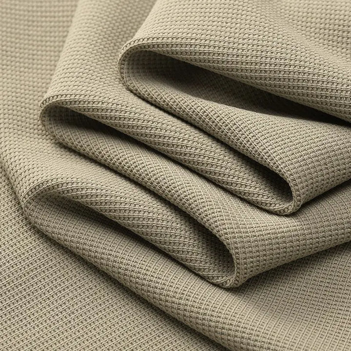 Close-up of several folds of light brown textured fabric with a waffle or honeycomb pattern, perfect for a wrinkle-resistant shirt, highlighting the fabric’s soft drape and detailed surface weave.