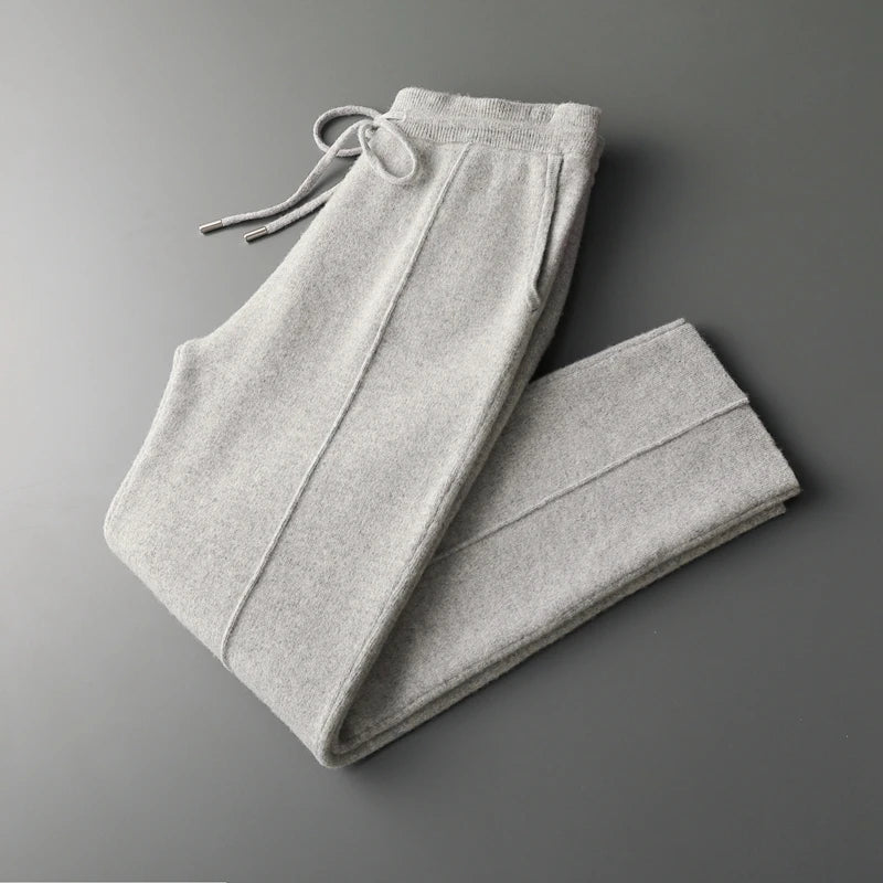 Light gray sweatpants neatly folded on a dark gray surface, featuring an elastic waistband with a drawstring and side pockets, crafted from a winter warm cashmere wool blend.