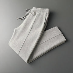 Light gray sweatpants neatly folded on a dark gray surface, featuring an elastic waistband with a drawstring and side pockets, crafted from a winter warm cashmere wool blend.