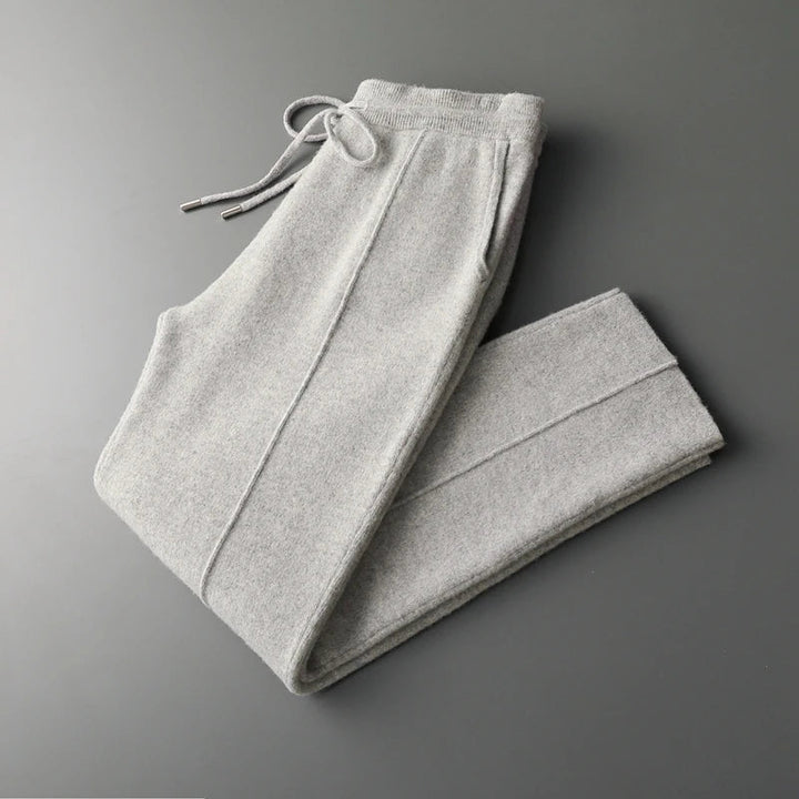 Light gray sweatpants neatly folded on a dark gray surface, featuring an elastic waistband with a drawstring and side pockets, crafted from a winter warm cashmere wool blend.