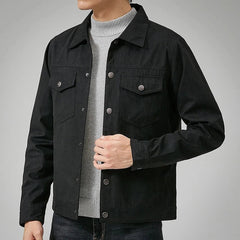 A person wearing a black velvet coat with a classic point collar over a light gray ribbed turtleneck sweater and dark jeans, standing against a plain gray background.