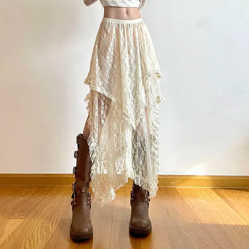 A person wearing a high-waist white lace asymmetrical skirt and brown knee-high boots stands indoors on a wooden floor against a plain white wall. Their upper body is cropped out of the image.