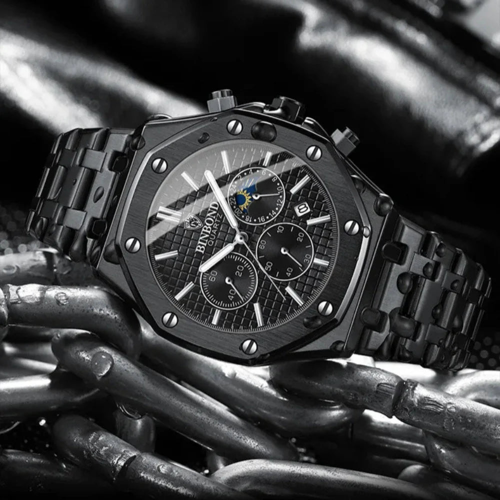 A luxury black stainless steel watch with a textured dial, chronograph dials, and silver hour markers rests on a pile of thick metal chains with a leather surface in the background.
