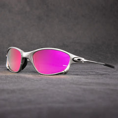 Sporty outdoor eyewear with silver frames and pink-purple mirrored lenses, offering UV protection, rests on a gray textured surface with a blurred gray background.