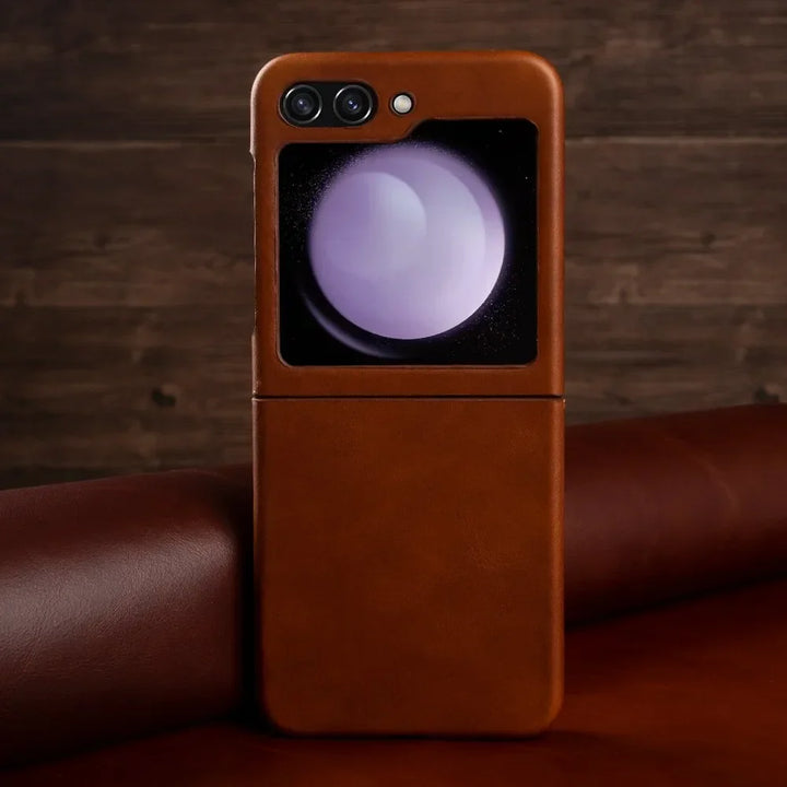 A genuine leather phone case covers a Samsung Galaxy Z Flip, which is partially open and resting on a brown surface. The phone’s external display shows a circular, purple-tinted graphic.