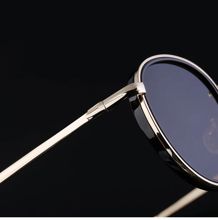 Close-up of rounded sunglasses with thin, gold-colored metal arms and dark tinted, scratch resistant lenses featuring UV400 protection, set against a black background.