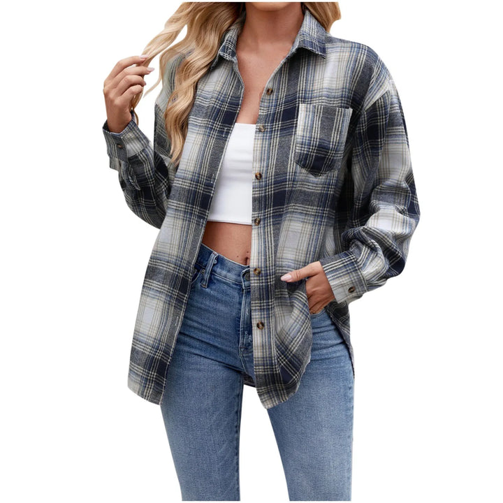 A woman wearing an oversized fit blue and grey plaid button-down shirt over a white crop top, layered with light blue jeans. She has long, wavy blonde hair and is posing with one hand near her hair.