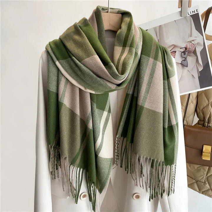 A white blazer on a hanger is draped with a lightweight, green, beige, and cream plaid scarf that has fringed ends. Photos of outfits are pinned to the wall in the background.