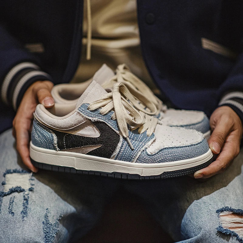 A person wearing ripped blue jeans and a dark jacket holds a pair of Denimwave 1986 Pro Sneakers with beige laces and textured fabric, resting them on their lap—capturing an effortless 80s aesthetic.