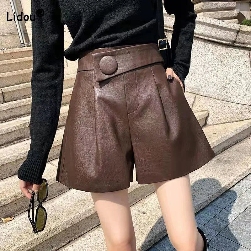 A person wearing high-waisted calfskin leather shorts with button detail and a black long-sleeve top stands outside on stone steps, holding sunglasses in one hand.