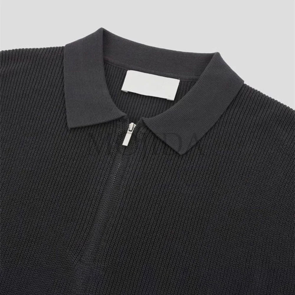 A close-up of a black quarter zip polo shirt with ribbed detailing and a collar, crafted in textured knit, displayed on a light gray background.