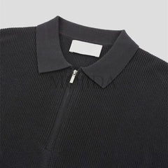 A close-up of a black quarter zip polo shirt with ribbed detailing and a collar, crafted in textured knit, displayed on a light gray background.