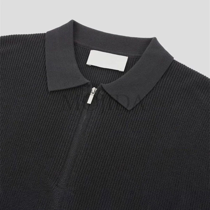 A close-up of a black quarter zip polo shirt with ribbed detailing and a collar, crafted in textured knit, displayed on a light gray background.