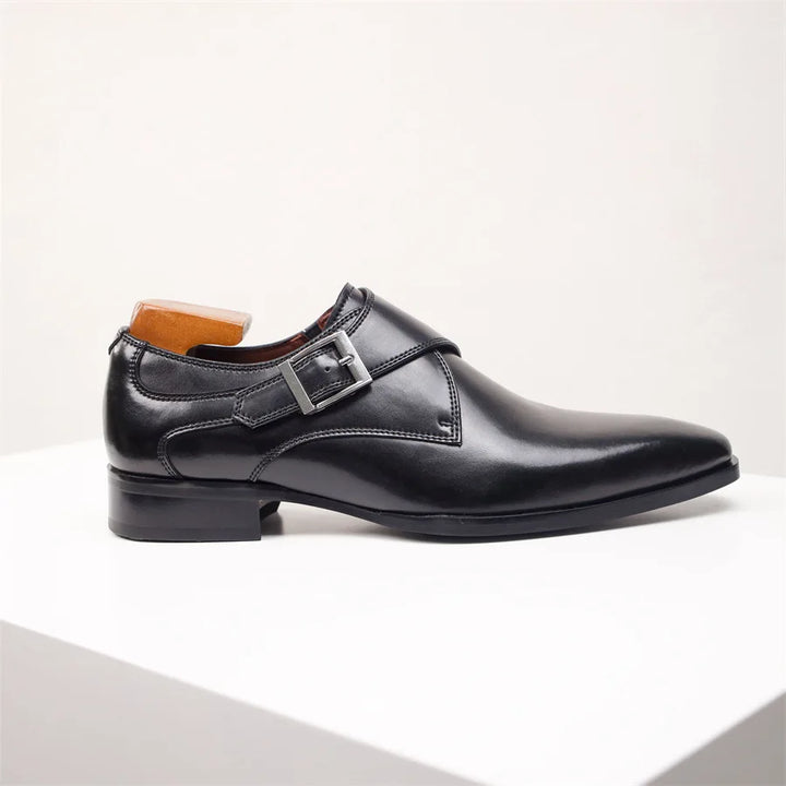A handcrafted black leather monk strap shoe with a silver buckle, made from premium Italian leather, displayed on a white platform against a plain light background.