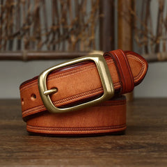 A genuine leather cowhide belt with visible stitching and a large brass buckle, coiled neatly on a wooden surface against a blurred background.