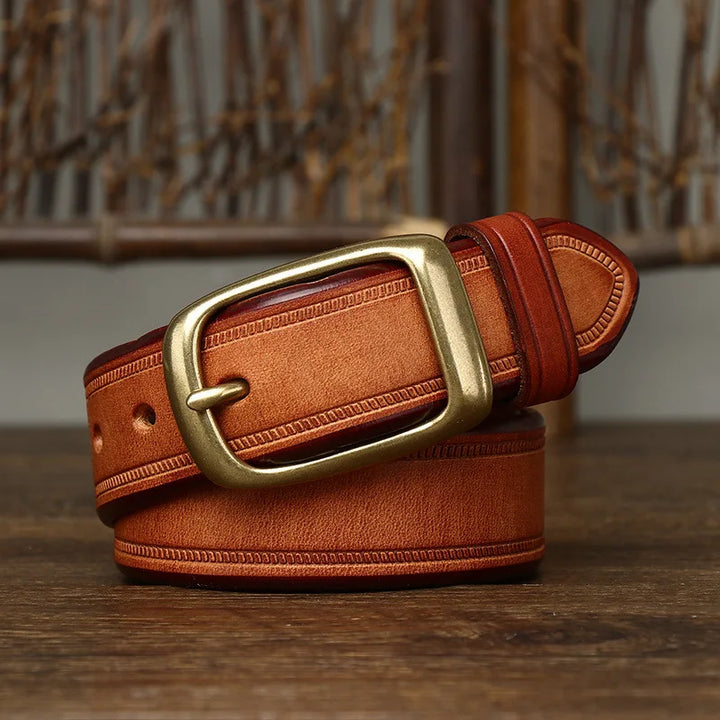 A genuine leather cowhide belt with visible stitching and a large brass buckle, coiled neatly on a wooden surface against a blurred background.