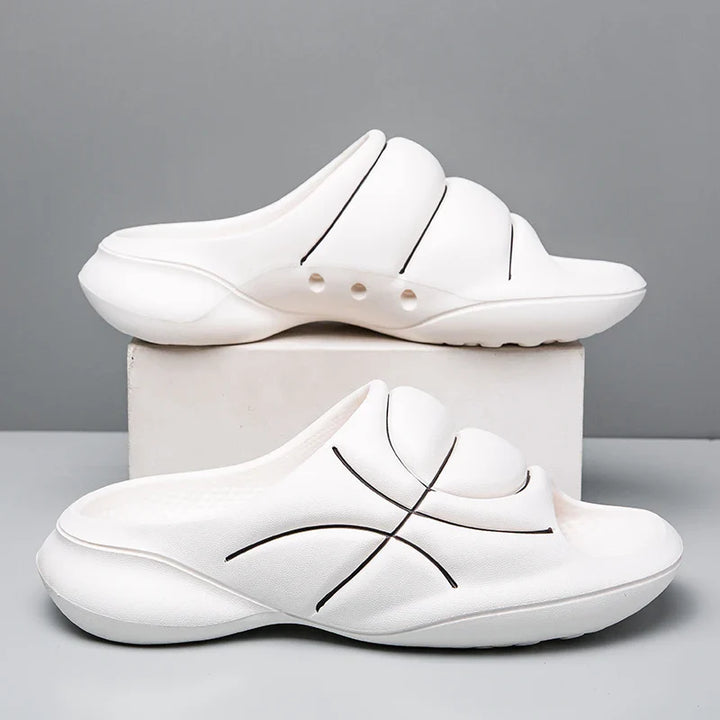 Two white slip-on sandals with a cushioned footbed and thick soles feature black curved line designs, displayed—one upright and one on its side—against a plain gray background, resembling the comfort of basketball slip ons.