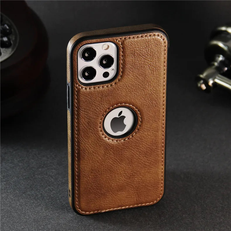 A smartphone with a luxury leather phone case stands upright on a dark surface. The slim protective case has a circular cutout revealing the Apple logo, with precise camera cutouts, and is wireless charging compatible. An old-fashioned phone is partially visible behind.