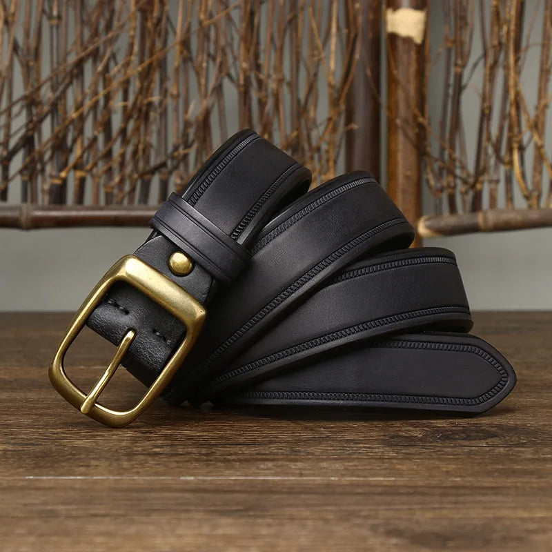 A black cowhide belt with a brass buckle is coiled on a wooden surface. A rustic, wooden decorative background featuring twigs is visible behind this genuine leather accessory.