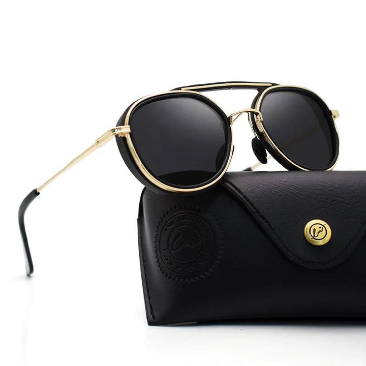 A pair of round, gold-framed polarized sunglasses with black lenses is displayed resting on a closed black leather case with a button closure and embossed logo.