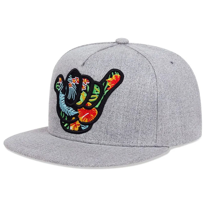 A light gray tropical snapback featuring an embroidered shaka hand symbol adorned with colorful tropical floral patterns on the front, perfect for a Hawaiian-inspired look.