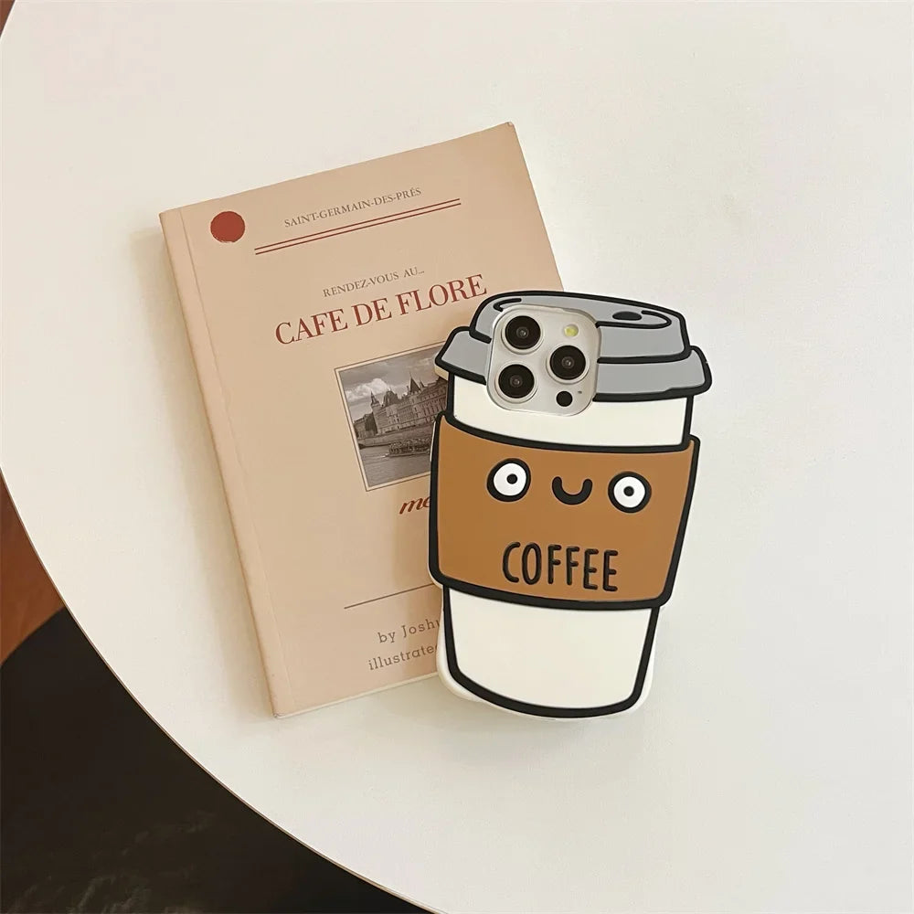 A beige book titled Café de Flore lies on a white round table beside a phone in a cute 3D coffee cup-shaped case, made of soft silicone for shockproof protection, with a smiling face and the word coffee on its sleeve.
