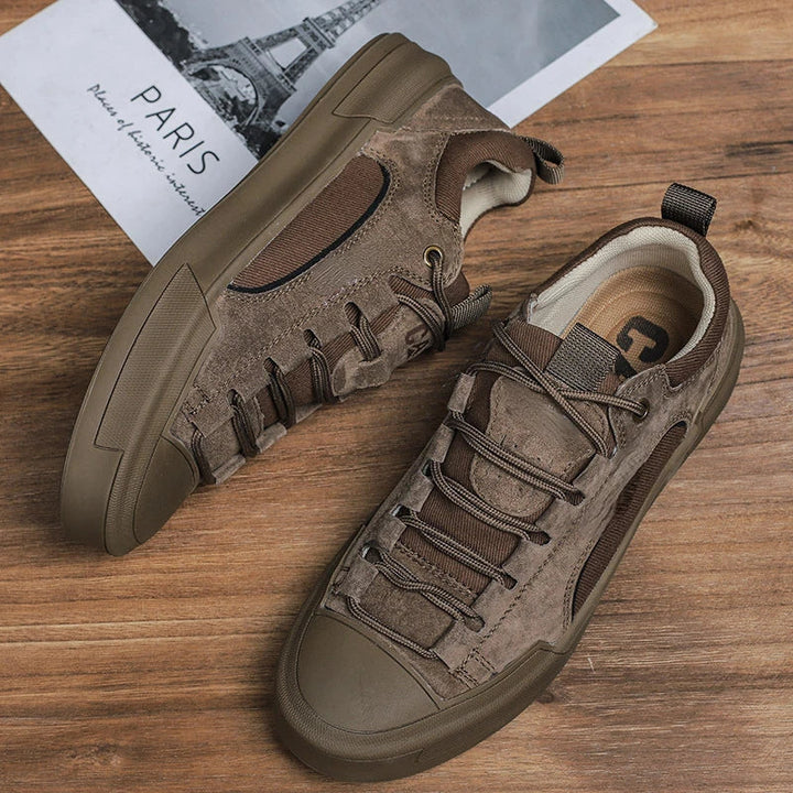 A pair of brown suede canvas shoes with mesh details and a cushioned insole sit on a wooden floor next to a grayscale photo of the Eiffel Tower labeled PARIS.