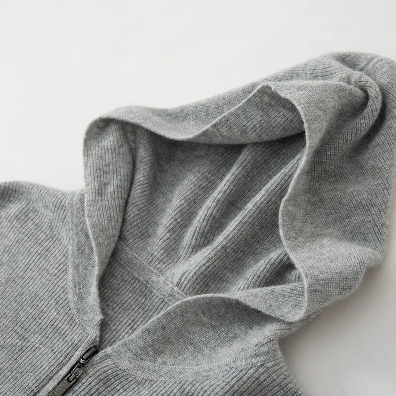 A close-up of a light gray, ribbed knit cashmere hoodie with a zipper, showing the luxurious cashmere texture and lightweight insulating fabric, with the hood laid flat on a white surface.