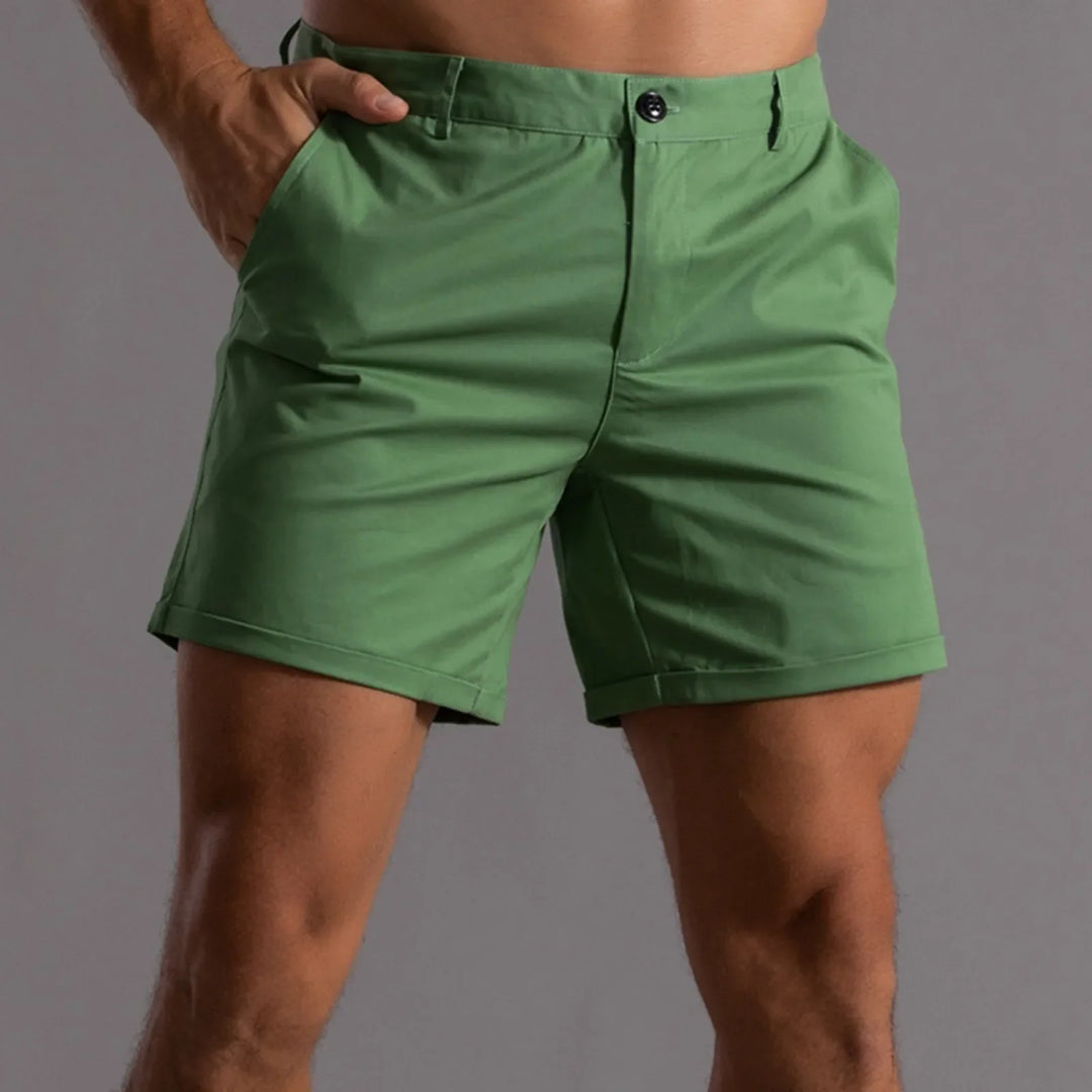 A person wearing green shorts with a semi elastic waistband and tailored fit, one hand in their pocket, shown from the waist to mid-thigh against a plain gray background.