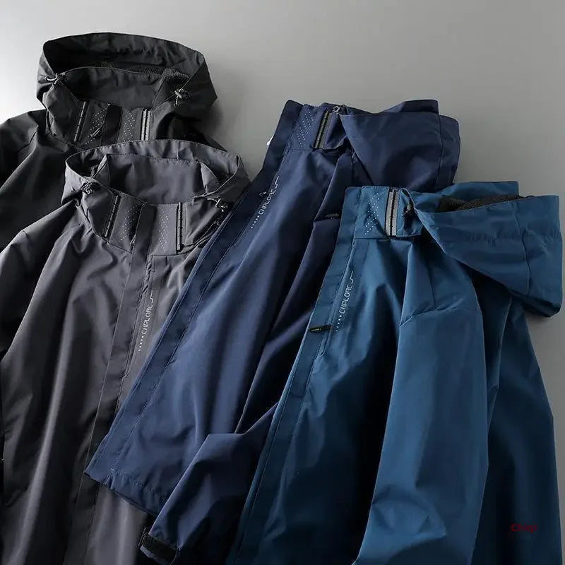 Three hooded jackets—a windproof jacket in dark gray, navy blue, and teal—are laid flat on a light gray surface, showcasing their hoods, zippers, and seam details.