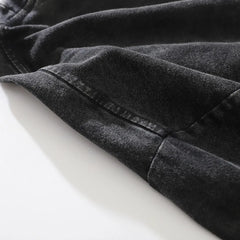Close-up of a black denim fabric made from premium cotton with visible stitching along a seam, lying flat on a white surface. The texture and weave of the material are clearly shown.