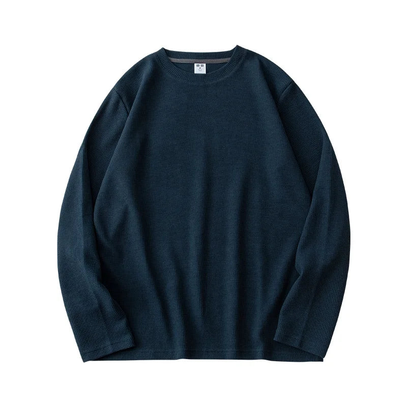 A dark blue, heavyweight long-sleeve shirt with a crew neck is laid flat on a white background. The ribbed fabric resembles waffle knit, giving it a distinctly textured look.