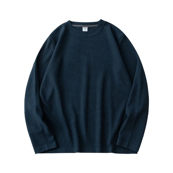 A dark blue, heavyweight long-sleeve shirt with a crew neck is laid flat on a white background. The ribbed fabric resembles waffle knit, giving it a distinctly textured look.