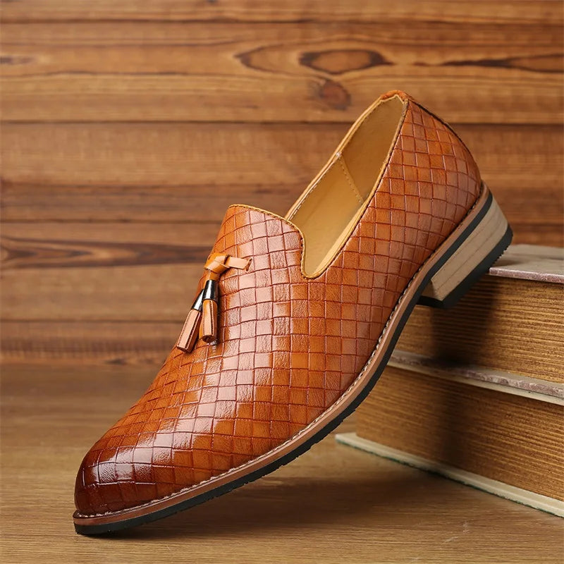 A single brown basketweave pattern loafer with a tassel detail, crafted from real leather shoes, displayed on top of stacked books against a wooden background.