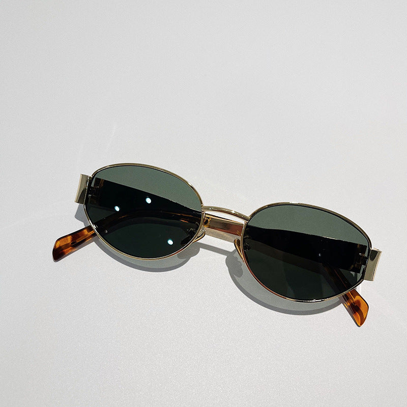 A pair of vintage-inspired, oval-shaped sunglasses with dark UV400 protection lenses, gold metal frames, and brown tortoiseshell arms, placed on a light-colored surface.