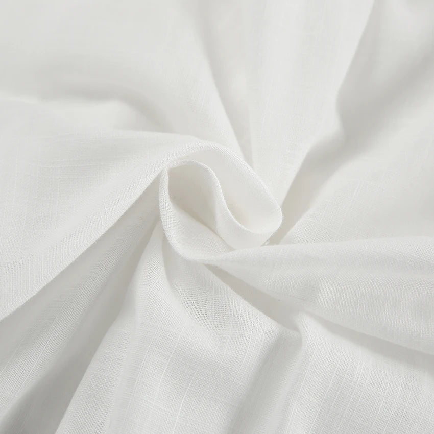 Close-up of soft, white fabric with a subtle texture, gently gathered and twisted in the center—perfect for a chic romper, adding natural folds and smooth flow ideal for a stylish summer outing.