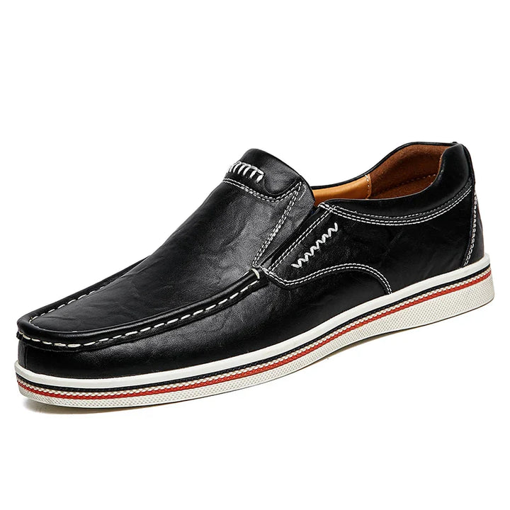 A black leather slip-on loafer with white stitching, a white sole, and a red stripe accent along the edge. These boat-style loafers feature a light brown interior for added comfort.