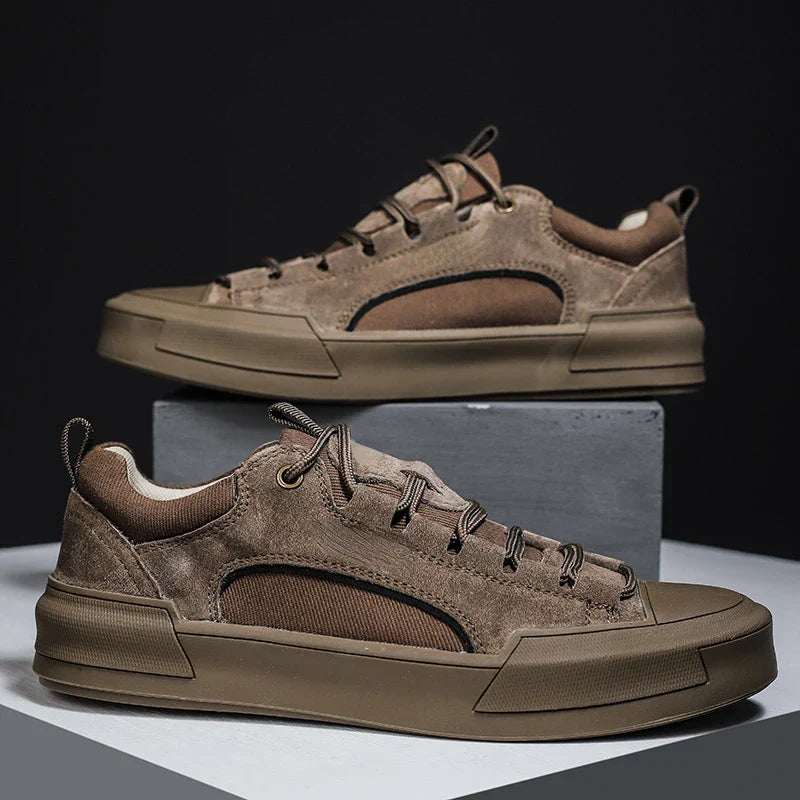 A pair of stylish brown suede canvas shoes with thick, durable rubber outsoles, displayed on and beside a gray block against a dark background.