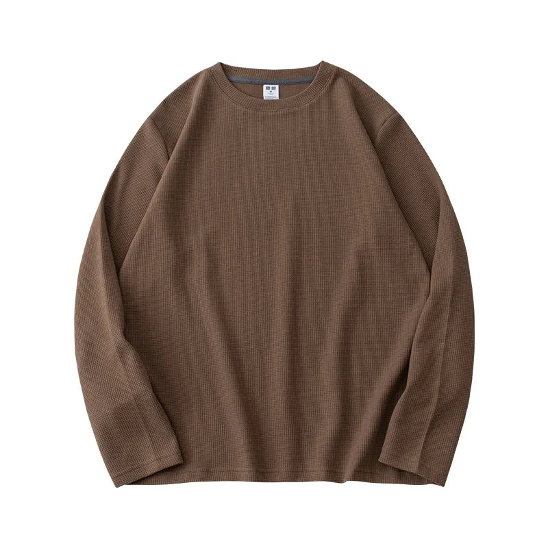 A long-sleeve, crew neck, brown waffle knit sweater is laid flat on a white background. The premium cotton fabric features a subtle textured pattern, and a small white tag is visible at the neckline.