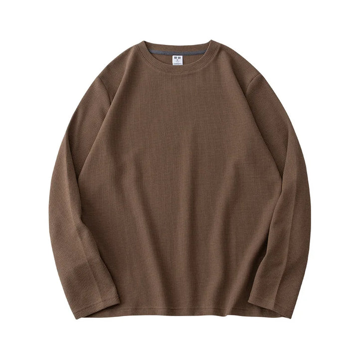 A long-sleeve, crew neck, brown waffle knit sweater is laid flat on a white background. The premium cotton fabric features a subtle textured pattern, and a small white tag is visible at the neckline.