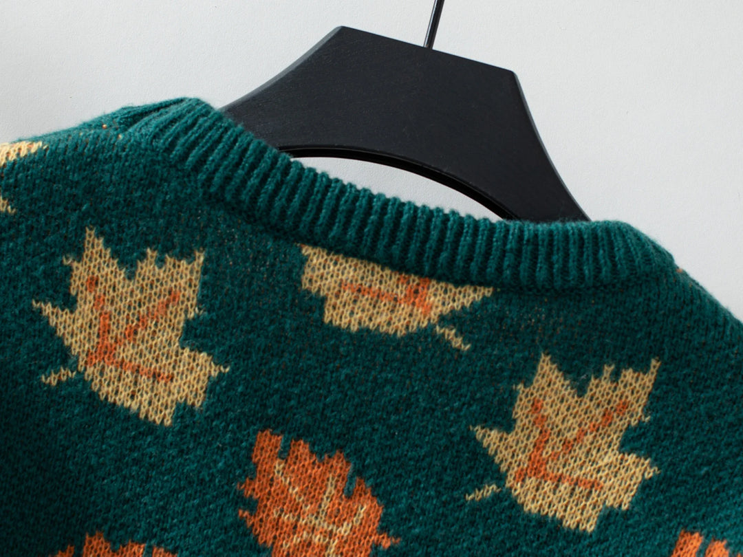 A close-up of a comfortable sweater made from soft knit material, featuring orange and beige maple leaf patterns, displayed on a black hanger against a light background.