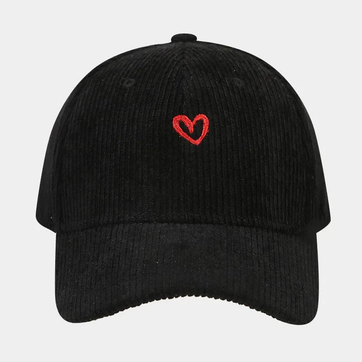 A black corduroy baseball cap featuring a small, red heart embroidery on the front center and a comfortable FlexFit band for a perfect fit.