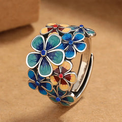 A silver ring decorated with vibrant colors in enamel flower designs—blue, yellow, and red—arranged closely together. The background is a warm brown surface.