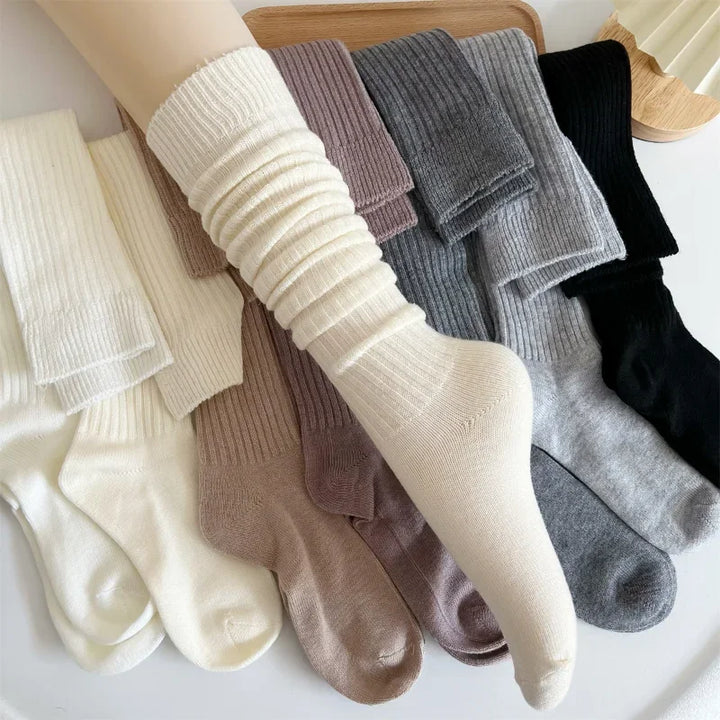 A display of ribbed, cozy socks in various colors—cream, brown, gray, and black—crafted from a Cashmere cotton blend for superior insulation, arranged neatly on a surface with one cream sock modeled on a mannequin leg in the center.