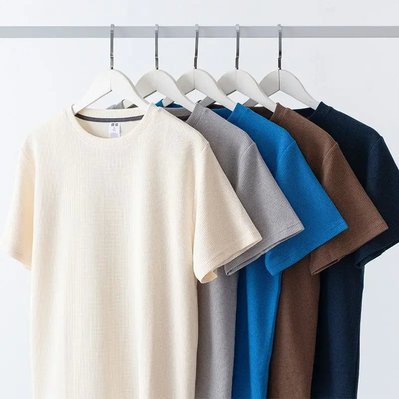 Five short-sleeved waffle knit shirts in cream, light gray, blue, brown, and navy hang neatly on white hangers against a plain white background—crafted from high-quality cotton for a breathable shirt youll love to wear.