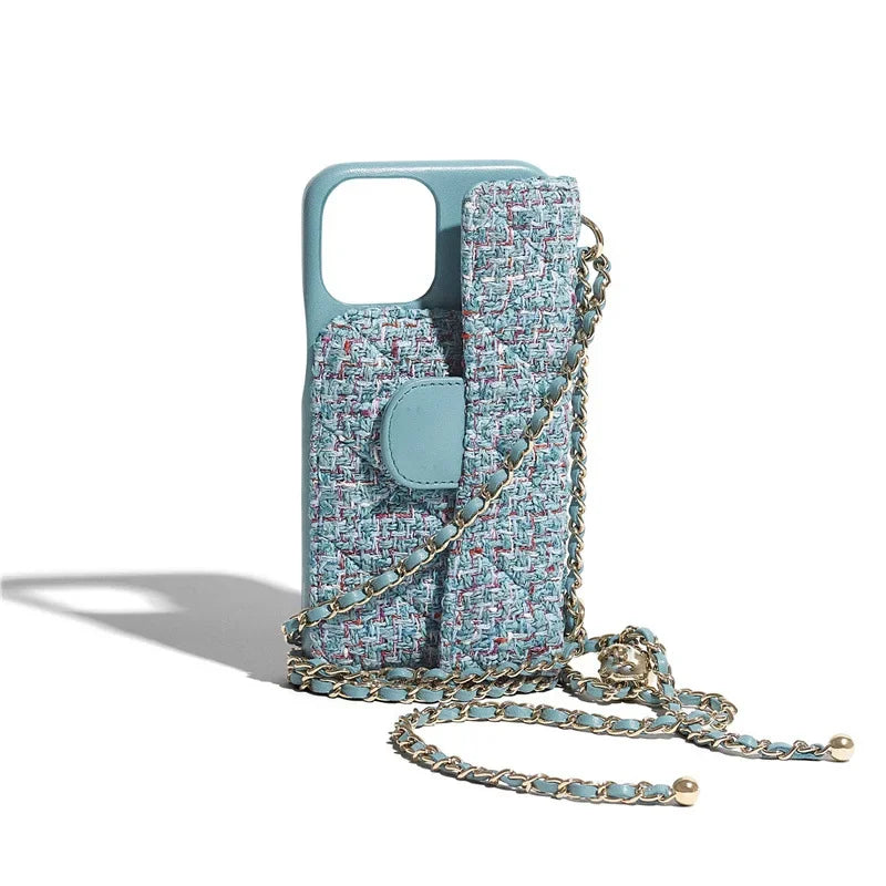 A stylish blue and pink tweed quilted phone case with a matching strap and gold chain accents, designed to be worn crossbody. The case is standing upright with the stylish chain strap laid out in front.