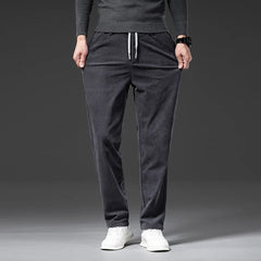 A person wearing dark gray men's smart casual pants with a drawstring, a matching long-sleeve shirt, and white sneakers stands against a plain dark background. Their hands are in their pockets.
