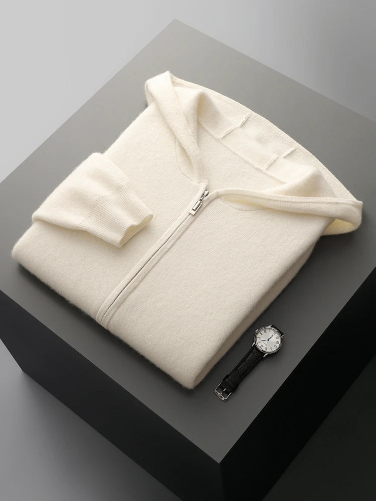 A cream-colored zip-up hoodie is neatly folded on a dark gray surface next to a black leather wristwatch with a white face, creating a cozy autumn winter cardigan vibe.