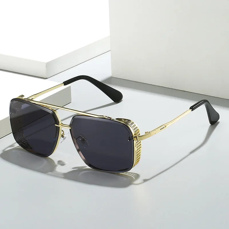 A pair of gold-framed, rectangular limited-edition sunglasses with dark tinted lenses and black temple tips, placed on a white surface with geometric shadows in the background.